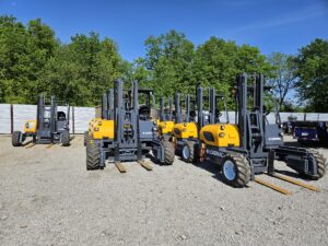 Loadmac truck-mounted forklifts lined up in a gravel yard, showcasing their robust design and dual reach capabilities, emphasizing versatility for heavy lifting and transportation.