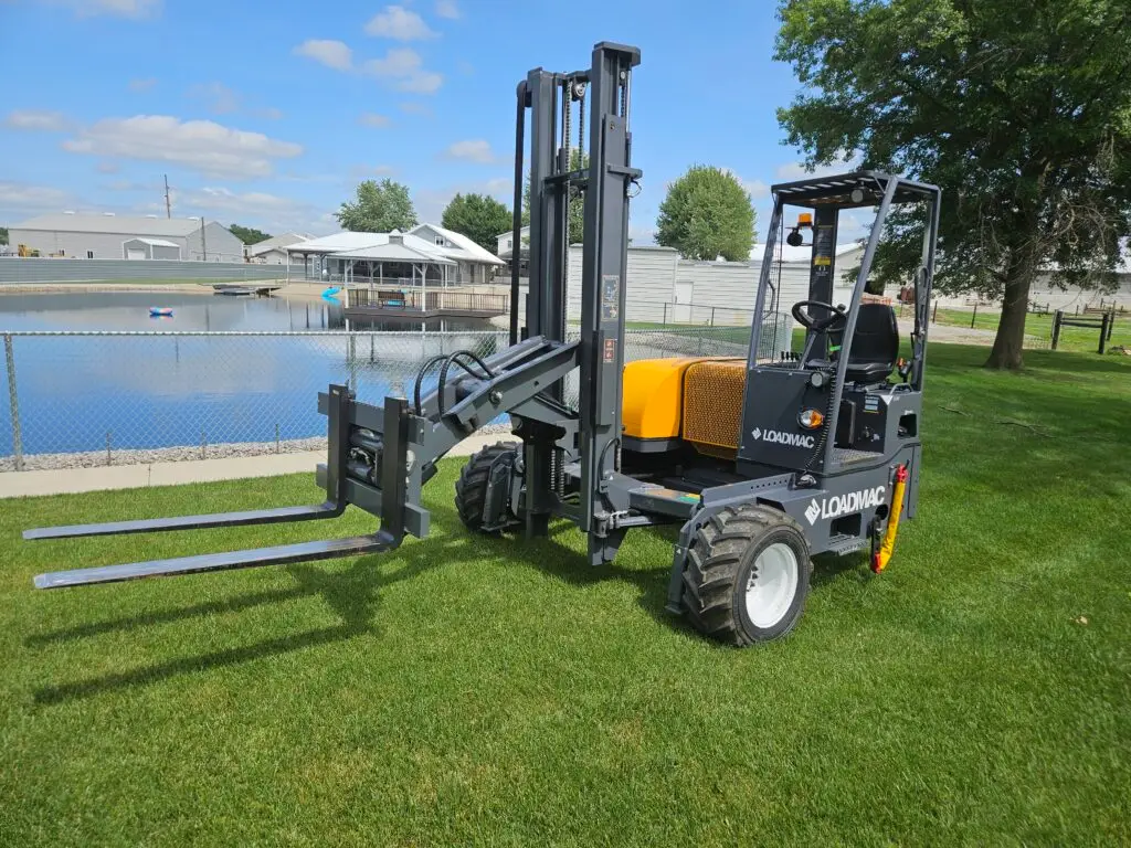 Loadmac truck-mounted forklift with double reach feature, positioned on grass near a pond, showcasing its maneuverability and design for heavy lifting and transportation.