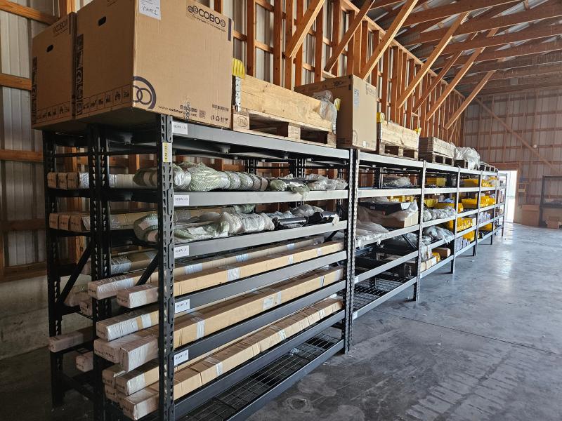 Loadmac parts displayed on shelves in a warehouse, showcasing various components essential for truck-mounted forklifts, including boxes and wrapped items for maintenance and repairs.