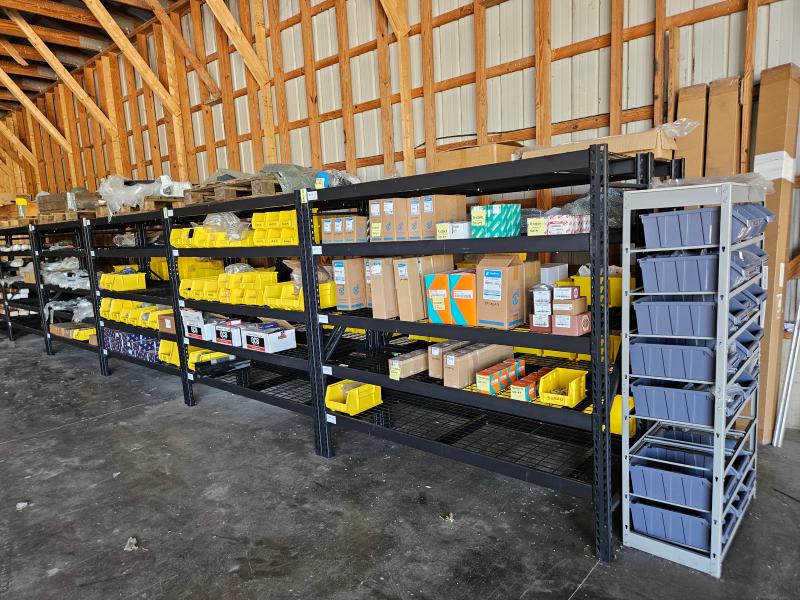 Warehouse shelves stocked with Loadmac forklift parts, including yellow bins and cardboard boxes, showcasing a variety of genuine parts for maintenance and repair.