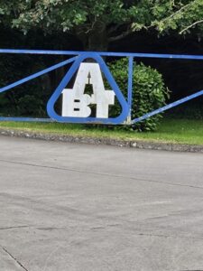 ABT Loadmac entrance gate featuring the company logo, surrounded by greenery and paved surface, symbolizing innovation in truck-mounted forklifts.