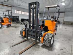Used Moffett M55 forklift with a raised mast and forks, showcasing durable construction and off-road tires, in a warehouse setting.